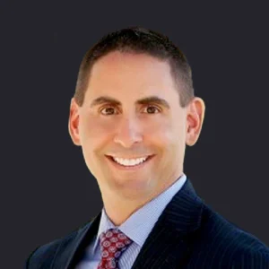 Craig Compiano, CEO in a dark suit with a blue shirt and red tie, smiles confidently against a plain black background.